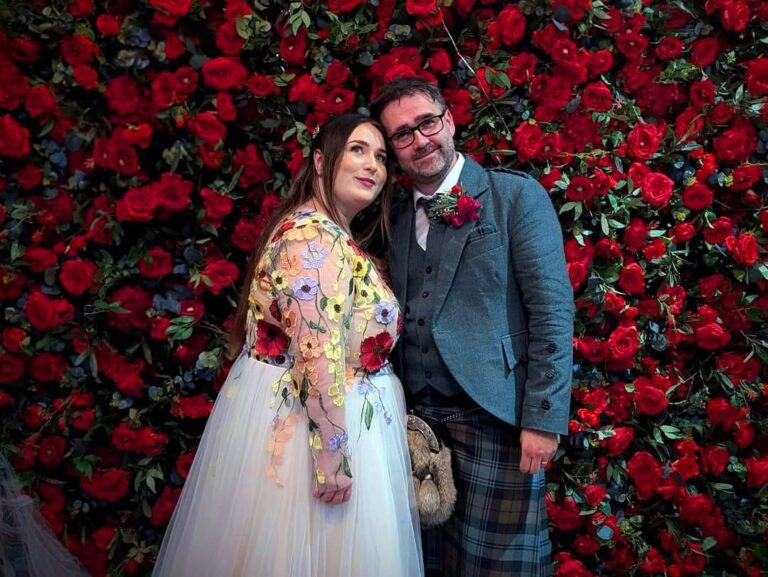 Paul in traditional Scottish Kilt and jacket, and Charlotte in a beautiful champagne colour wedding dress with red, orange, yellow and lavendar floral motif